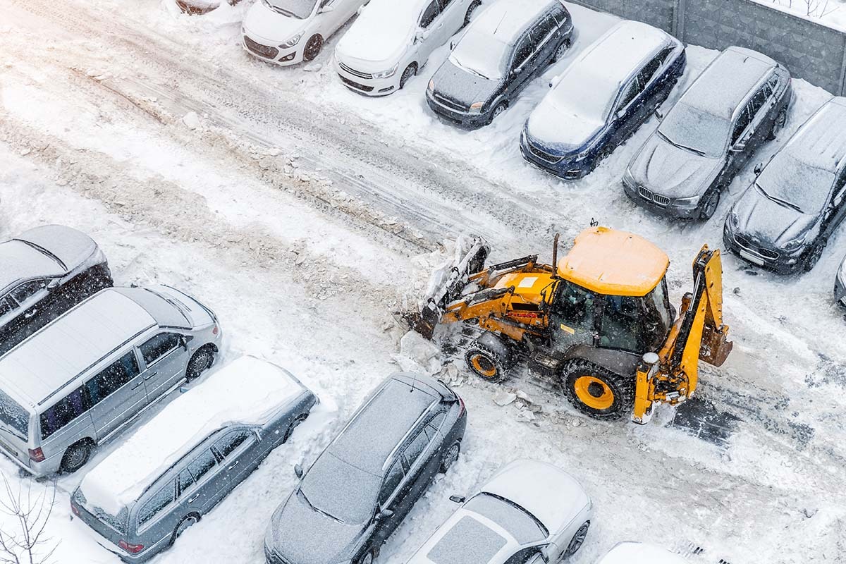 Tractor loader machine uploading dirty snow into dump truck. Cleaning city street, removing snow and ice after heavy snowfalls and blizzard. Snowplow outdoors clean pavement sidewalk road driveway